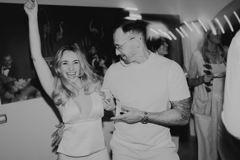 Fröhliches Paar tanzt auf einer Party, die Frau jubelt mit erhobenem Arm.