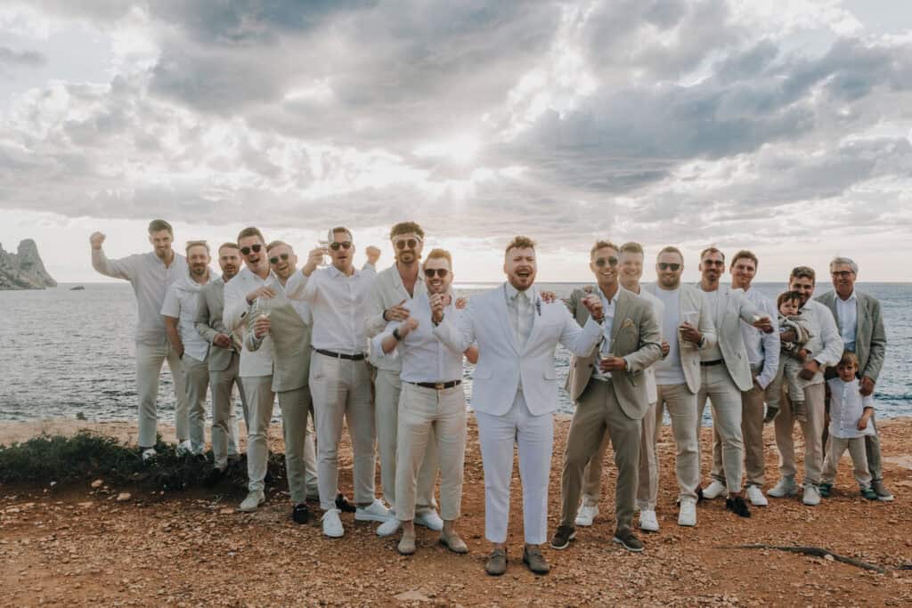 Groomsmen feiern Hochzeit auf Ibiza mit Meerblick und hellen Anzügen.