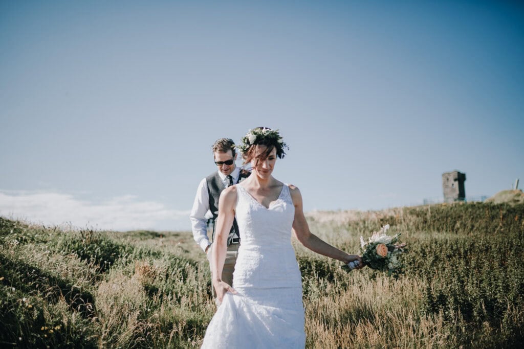 Brautpaar in Irland wandert durch grüne Landschaft. Die Braut trägt ein Blumenkranz. Hochzeitsfotograf Irland.