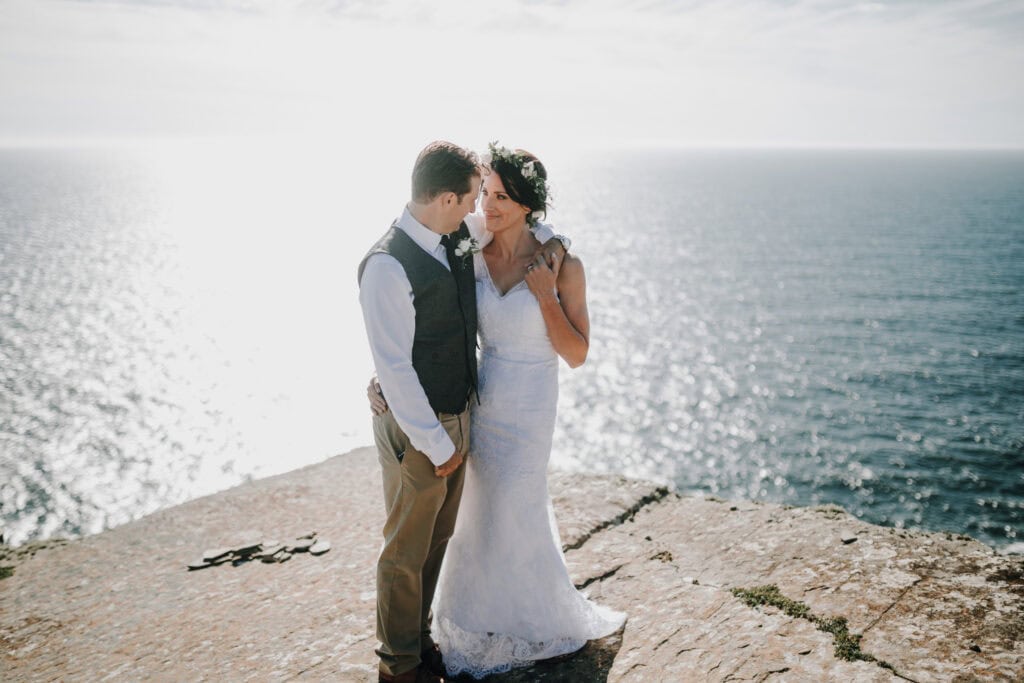 Brautpaar umarmt sich auf Klippe in Irland mit Meerblick. Romantische Hochzeit.