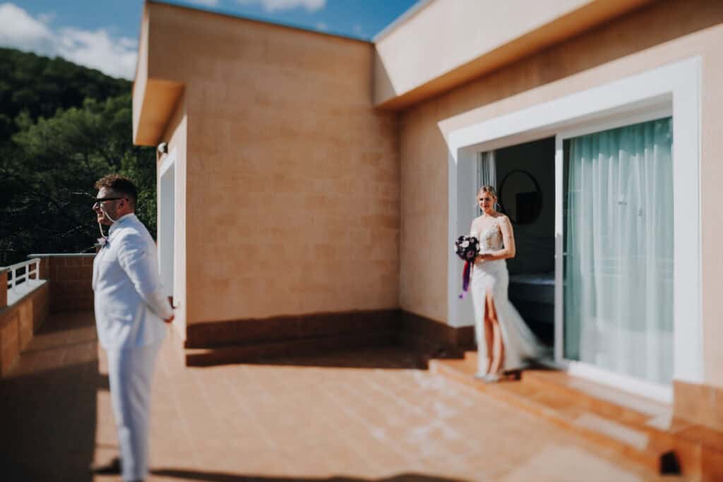 Brautpaar auf Ibiza: Braut im Kleid mit Blumenstrauß, Bräutigam im weißen Anzug auf Terrasse.