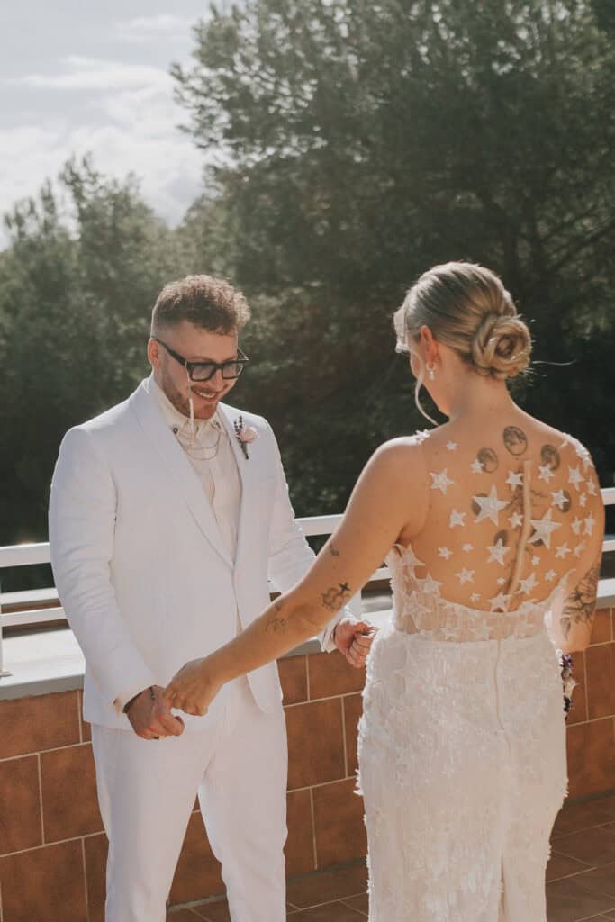 Bräutigam im weißen Anzug und Braut mit Sternenkleid halten Hände.