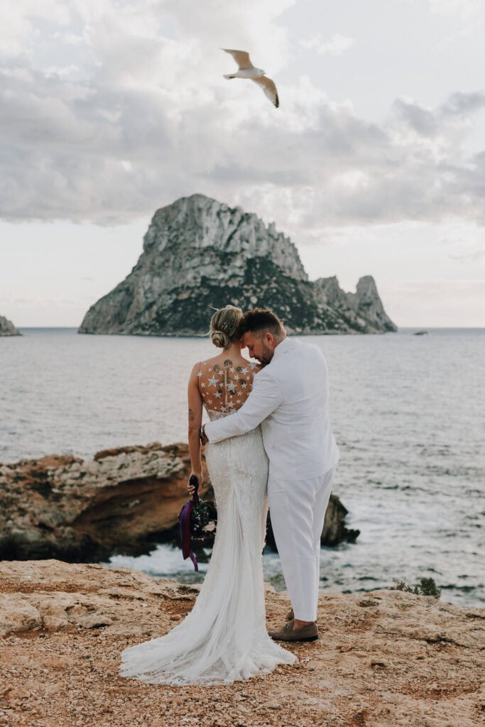 Brautpaar umarmt sich auf Ibiza vor Felseninsel Es Vedrà. Hochzeit am Meer. Hochzeitsfotograf Ibiza.