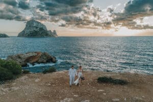 Brautpaar spaziert am Strand von Ibiza bei Sonnenuntergang mit Blick auf Es Vedrà. Romantische Hochzeit.