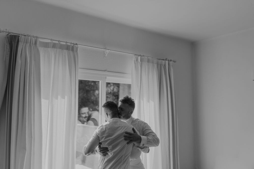 Zwei Männer umarmen sich vor einem Fenster.