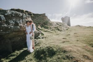 Brautpaar umarmt sich vor irischer Landschaft mit Turm. Blumenkranz und Brautstrauß.