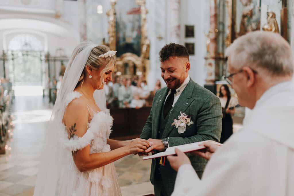 Brautpaar tauscht Ringe bei Hochzeit in Kirche. Bräutigam lächelt. Festliche Zeremonie.