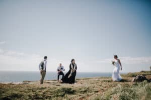 Brautpaar mit Gästen auf Klippe in Irland. Hochzeit im Freien, Meer im Hintergrund.
