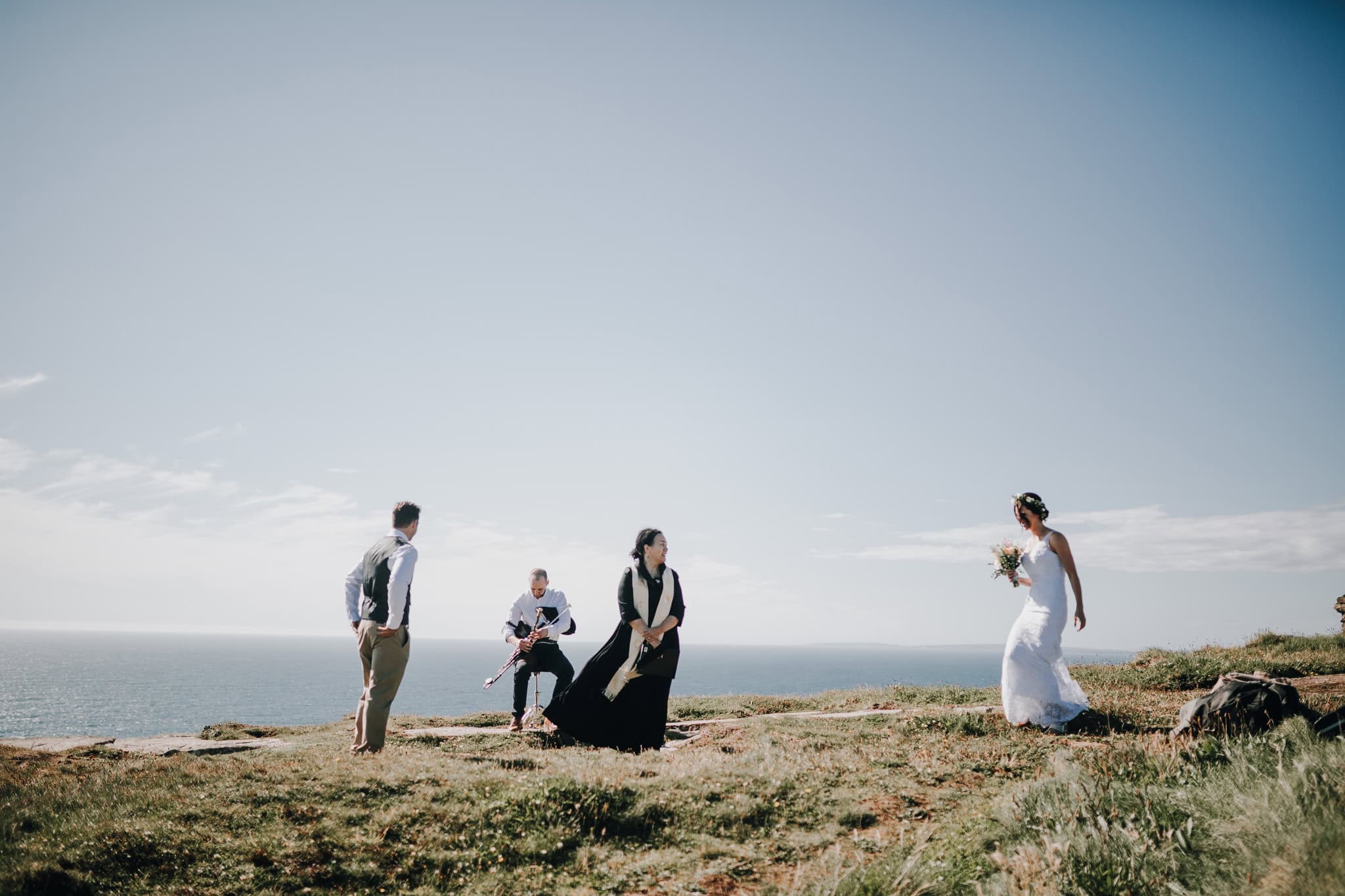 Brautpaar mit Gästen auf Klippe in Irland. Hochzeit im Freien, Meer im Hintergrund.