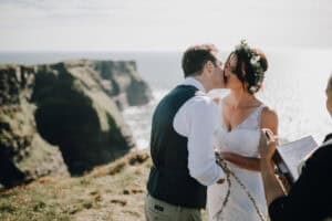 Brautpaar küsst sich vor den Cliffs of Moher, Irland. Blumenkranz, rustikale Hochzeit.