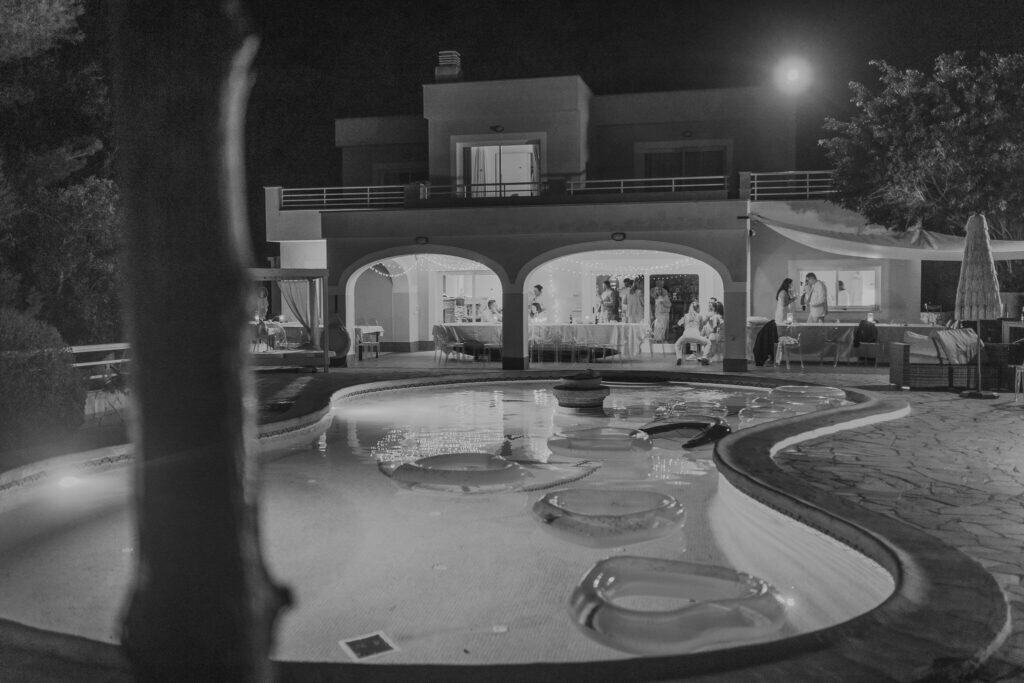 Hochzeitsfeier auf Ibiza: Poolparty im Freien mit beleuchtetem Haus und Gästen.