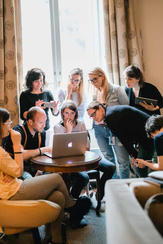 Gruppe schaut auf Laptop bei Workshop für Hochzeitsfotografen. Konzentrierte Menschen, heller Raum, Laptop mit Apfel-Logo.