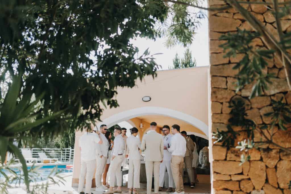 Hochzeitsgesellschaft in Ibiza versammelt sich unter einem Pavillon, gekleidet in Weiß und Beige.