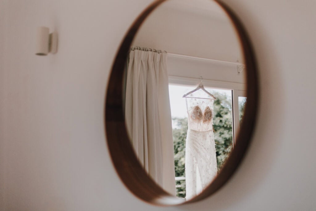 Hochzeitskleid hängt am Fenster, gesehen durch Spiegel. Eleganz und Vorfreude.
