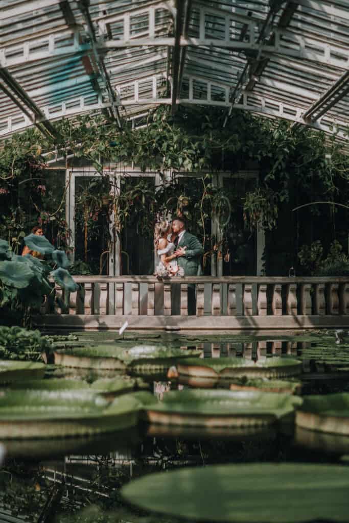 Hochzeitspaar küsst sich im Gewächshaus mit Seerosenbecken. Romantische Hochzeitsfotografie München.