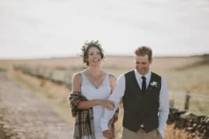 Glückliches irisches Hochzeitspaar geht Hand in Hand auf dem Land. Braut mit Blumenkranz und Schal.