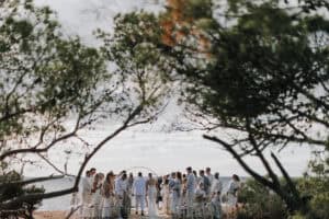 Hochzeitszeremonie im Freien auf Ibiza mit Brautpaar, Gästen und Meerblick unter Bäumen.