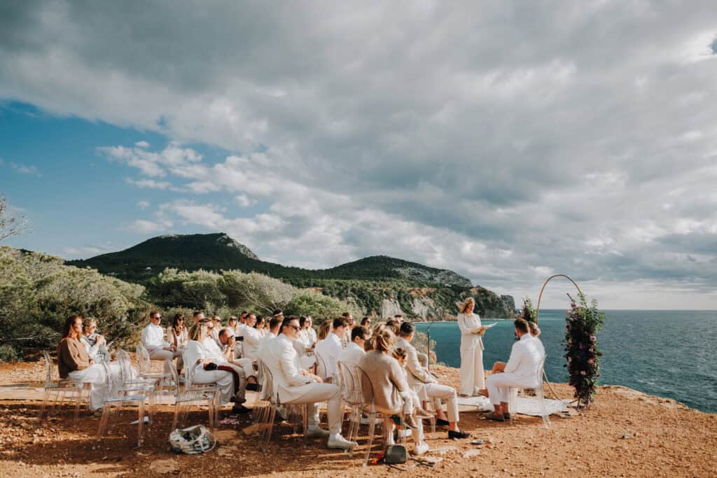 Hochzeitszeremonie im Freien auf Ibiza mit Brautpaar, Gästen in Weiß und Meerblick.