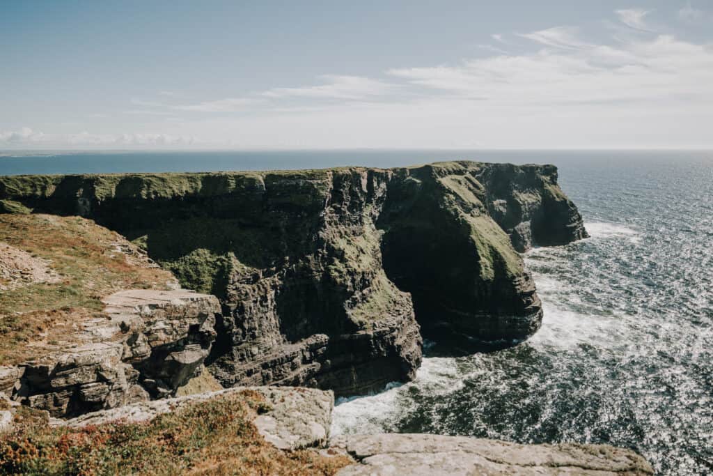 Dramatische Klippen von Irland am Meer mit schäumenden Wellen unter blauem Himmel.