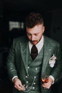 Mann im grünen Anzug mit Taschenuhr und Weinglas. Elegantes Outfit.