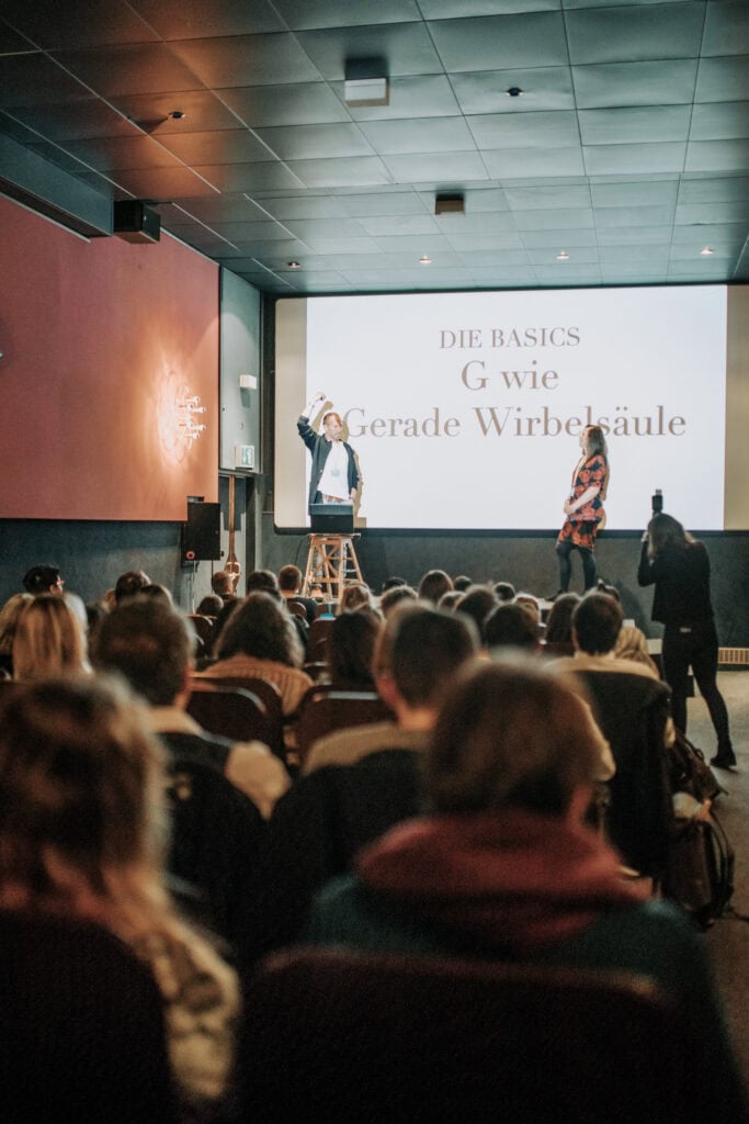 Workshop mit Vortrag über "G wie Gerade Wirbelsäule" vor Publikum. Hochzeitsfotografen lernen.