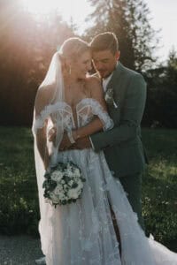 Brautpaar umarmt sich im goldenen Licht. Braut mit Blumenstrauß. Hochzeitsfotograf Tirol.