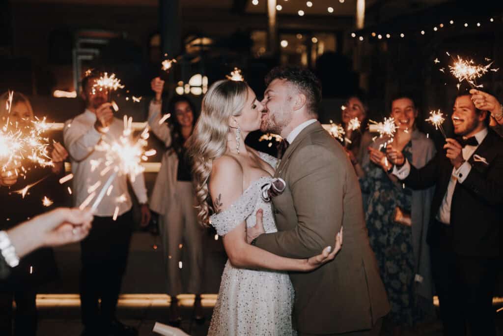 Brautpaar küsst sich bei Hochzeit mit Wunderkerzen. Hochzeitsfotograf Tirol. Romantisch, festlich.