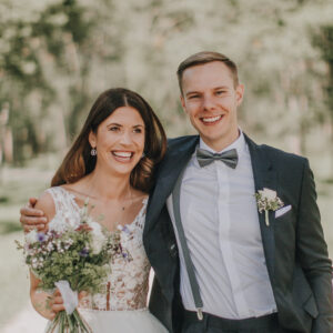 Glückliches Brautpaar im Freien. Braut hält Blumenstrauß, Bräutigam im Anzug. Hochzeitsfotograf Tirol.