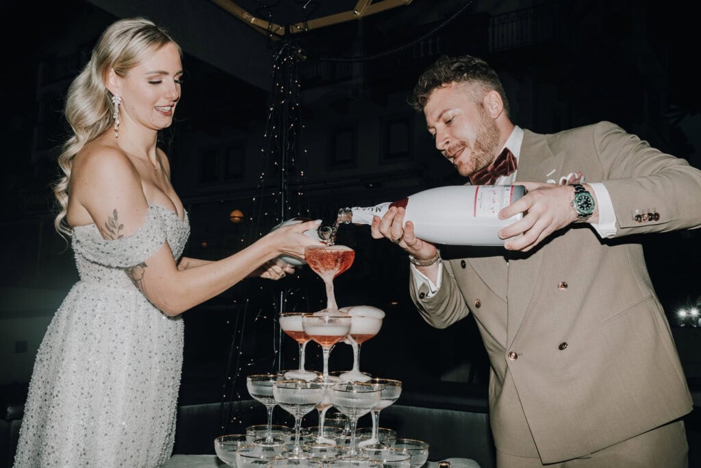 Brautpaar gießt Champagner in Gläserpyramide. Hochzeit in Tirol.