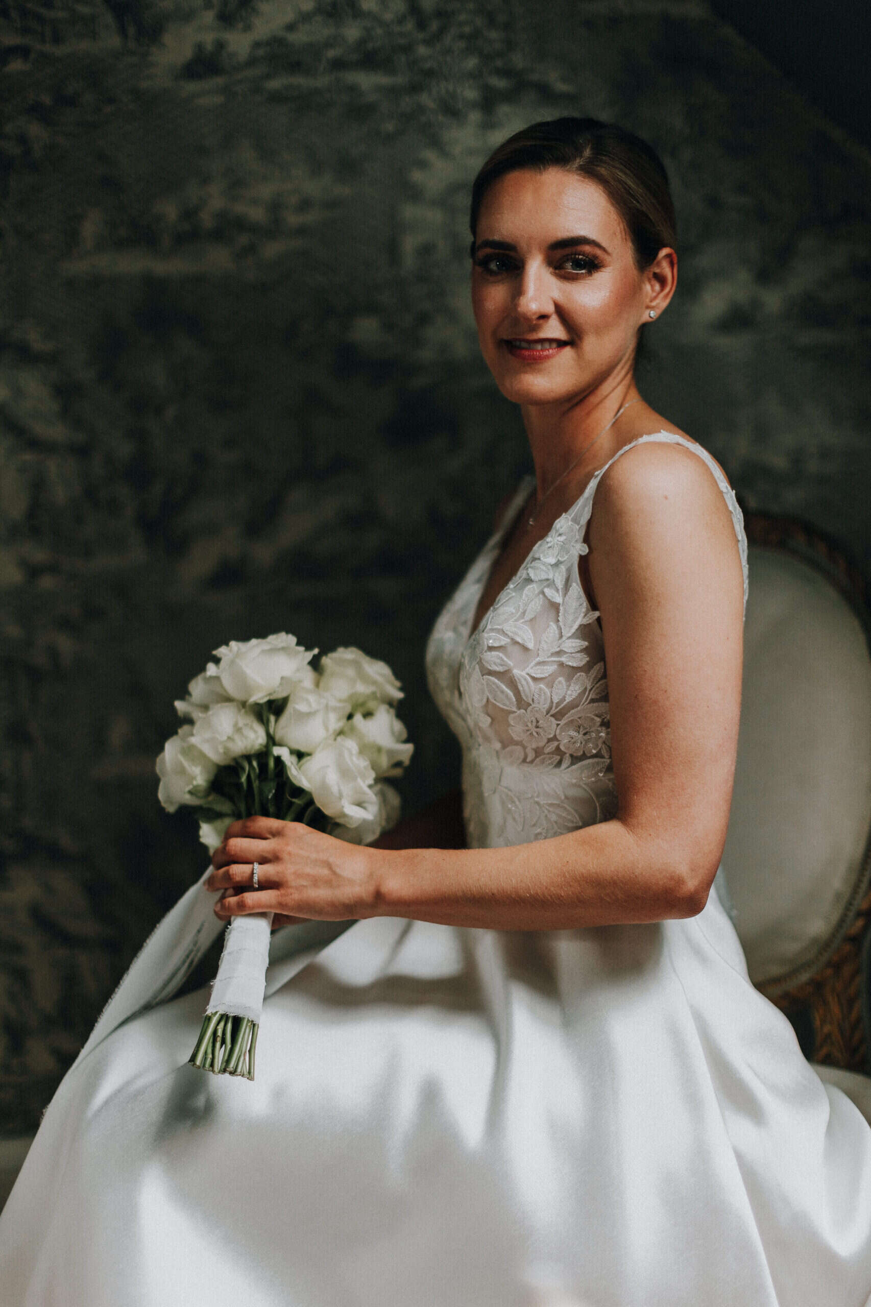 Elegante Braut mit weißem Rosenstrauß, sitzend. Hochzeit Tirol.