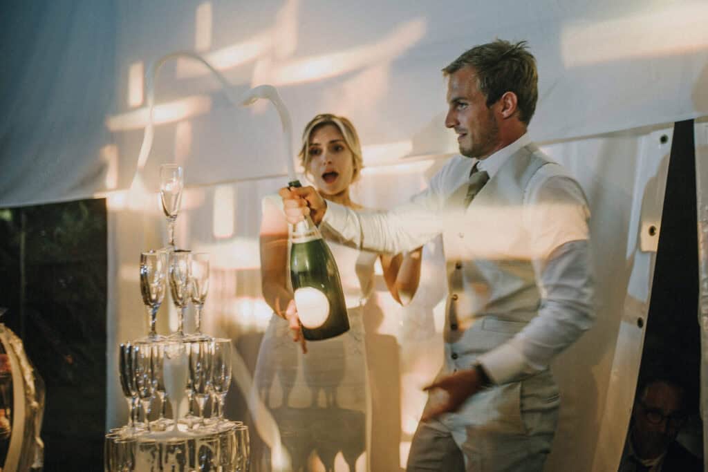 Bräutigam öffnet Champagner vor Hochzeitsturm, Braut schaut überrascht. Hochzeitsfotograf Tirol.