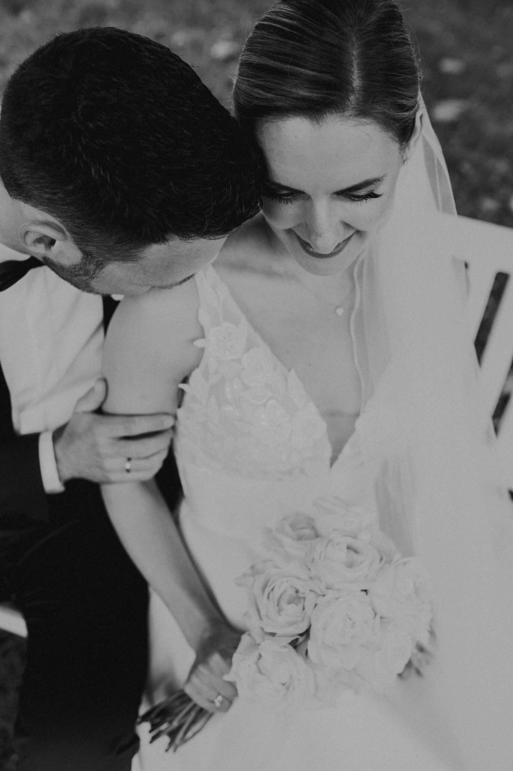 Brautpaar kuschelt auf Bank. Braut hält Rosenstrauß. Hochzeitsfotograf Tirol.