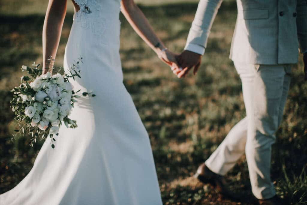Brautpaar hält Händchen mit Brautstrauß. Hochzeitsfotograf Tirol.