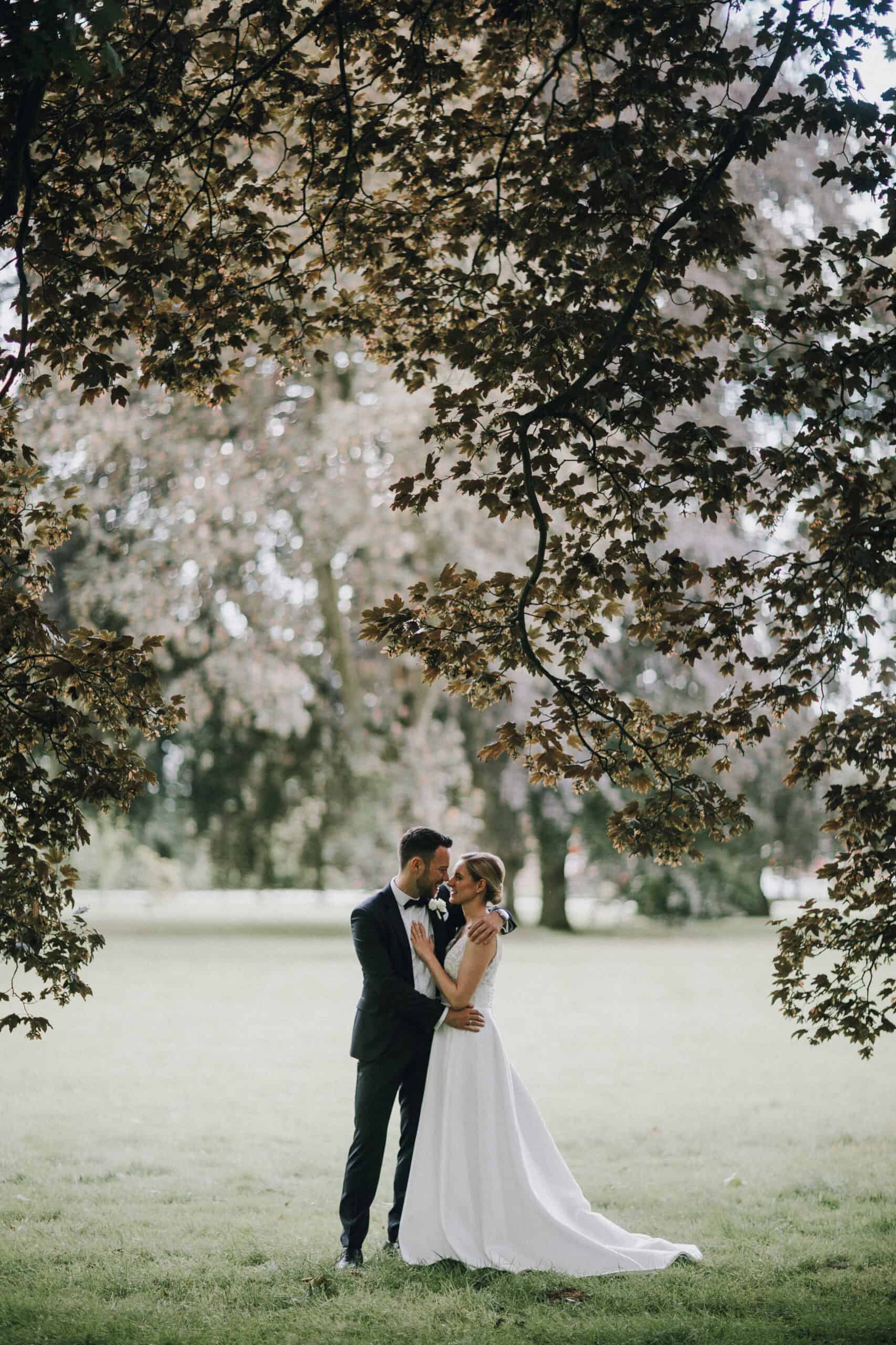 Brautpaar umarmt sich liebevoll unter einem Baum. Hochzeit im Grünen, Hochzeitsfotograf Tirol.