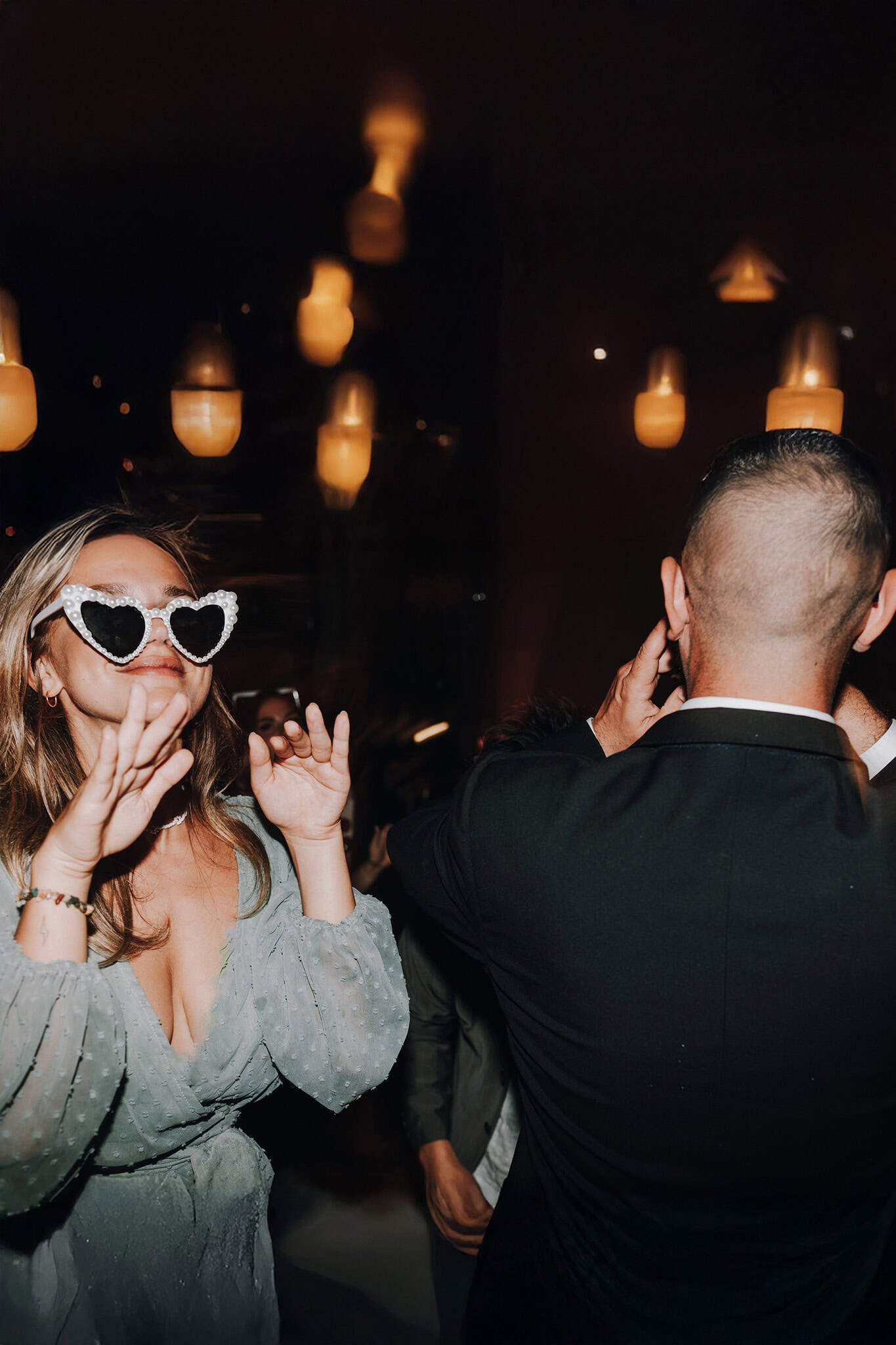 Frau mit Herzbrille tanzt auf einer Hochzeit. Stimmungsvolle Partybeleuchtung im Hintergrund.