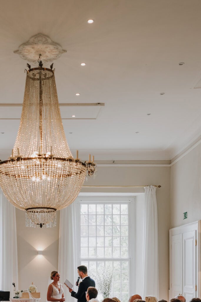 Hochzeitsszene unter Kronleuchter: Brautpaar bei Trauung in elegantem Saal.
