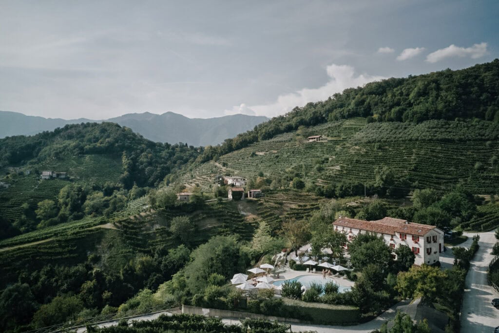 Italienische Landschaft mit Pool, Villa und Weinbergen. Hügelige Landschaft unter bewölktem Himmel.