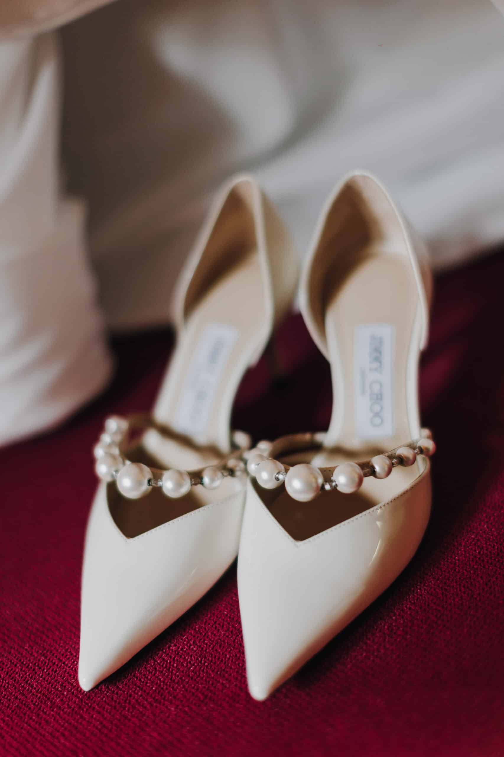 Elegante, weiße Jimmy Choo Brautschuhe mit Perlen auf rotem Stoff. Hochzeitsschuhe Detail.